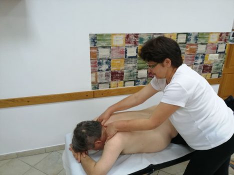 Medicinska masaža korisnika starije životne dobi. Na fotografiji čovjek leži na stolu za masažu, a maserka mu masira vrat.