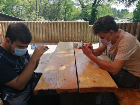 Na fotografiji dva slijepa muškarca sjede za stolom i rade na mobitelima.
