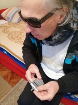 Na fotografiji muška osoba sjedi na krevetu i drži mobitel u ruci.