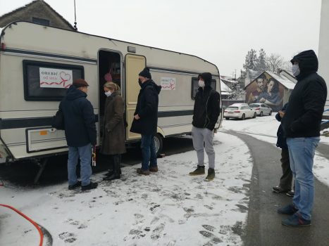 Na fotografiji se nalazi skupina ljudi pored kamp kućice.