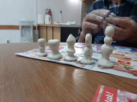 Na fotografiji se nalazi osoba koja od gline izrađuje šahovske figurice.