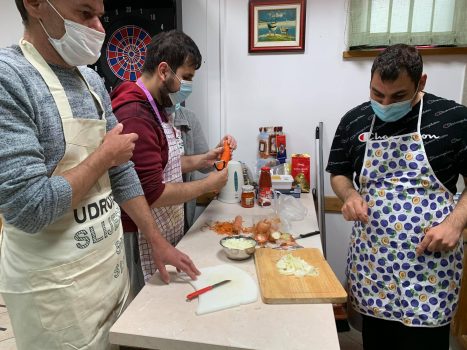 Na fotografiji se nalaze tri muške osobe, jedna muška osoba čisti mrkvu.