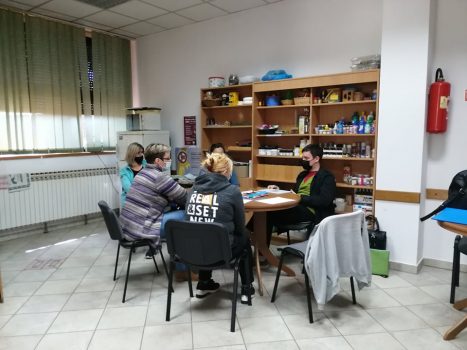 Na fotografiji se nalaze četiri ženske osobe i jedna muška osoba koji sjede na stolicama oko stola i razgovaraju.