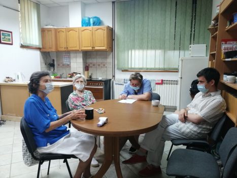 Na fotografiji skupina ljudi sjedi za stolom i razgovara na radionici psihosocijalne podrške.