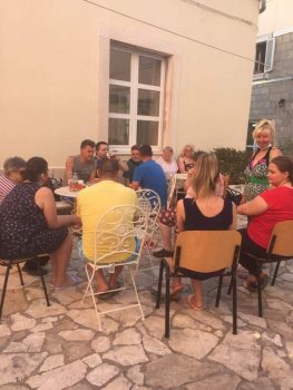 Na fotografiji se vidi skupina ljudi koja sjedi oko stola i veselo razgovara.