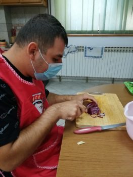 Na fotografiji se nalazi mlađa muška osoba koja sjecka ljubičasti luk na kulinarskoj radionici.