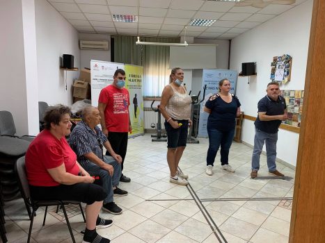 Na fotografiji se nalazi skupina ljudi, muška i ženska osoba igraju pikado