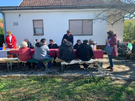 Na fotografiji skupina ljudi sjedi oko stolova u dvorištu kuće povodom obilježavanja Dana bijelog štapa.