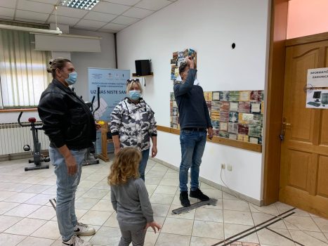 Na fotografiji se nalaze dvije ženske, muška osoba i dijete. Muška osoba baca strelicu prema pikadu.