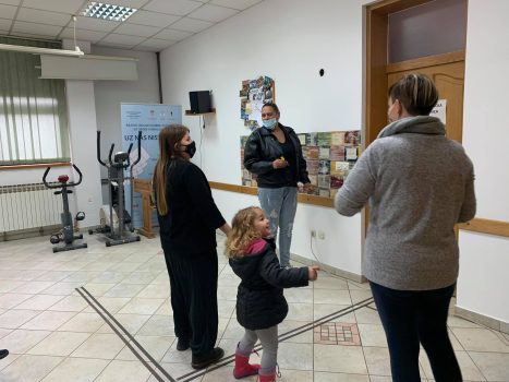 Na fotografiji se nalaze tri ženske osobe koje razgovaraju, a pored njih stoji dijete.