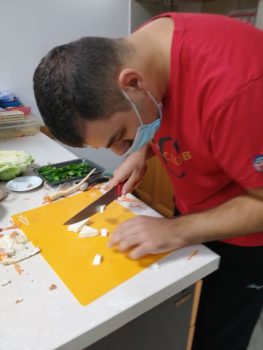 Na fotografiji mlađa muška osoba sjecka peršin i celer na kulinarskoj radionici.