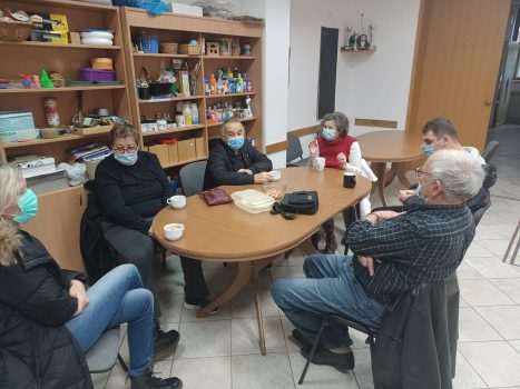 Na fotografiji tri ženske i tri muške osobe sjede za stolom i razgovaraju na radionici psihosocijalne podrške.