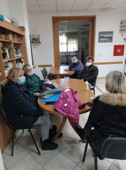 Na fotografiji tri ženske i dvije muške osobe sjede za stolom i razgovaraju na radionici psihosocijalne podrške.