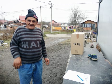 Na fotografiji se nalazi muška osoba, koja sa radošću prima paket pomoći od djelatnika Udruge slijepih.